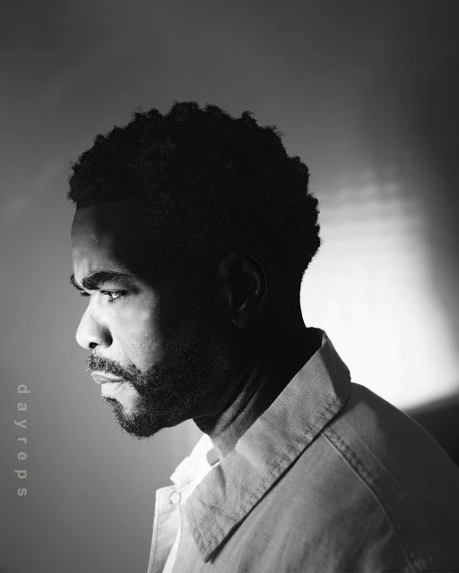 Monochromatic portrait of an African-American adult male with short curly hair and beard, looking off-camera, wearing a collared shirt.