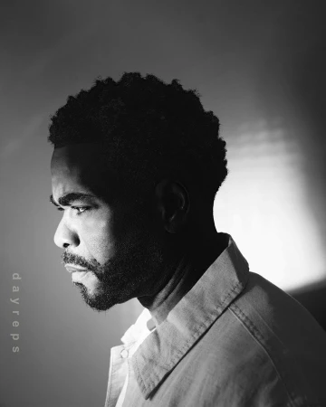Monochromatic portrait of an African-American adult male with short curly hair and beard, looking off-camera, wearing a collared shirt.