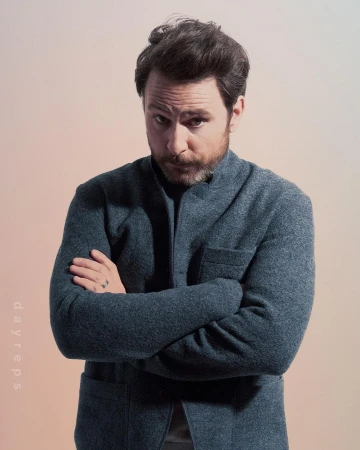 Portrait of a white man in his 40s wearing a grey jacket with arms crossed against a light gradient background