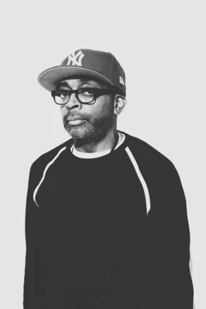 Portrait of Spike Lee wearing a baseball cap and thick-framed glasses in a black and white monochrome studio shot