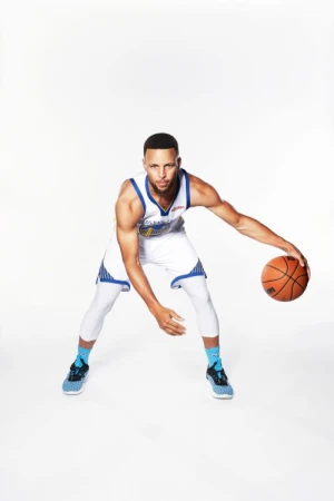 A male basketball player in a white and blue uniform dribbles an orange basketball in a brightly lit, minimalist photo studio.