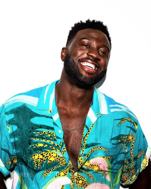 Close-up studio portrait of a smiling adult man with dark hair wearing a tropical print shirt against a clean white background.
