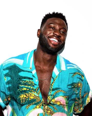 Close-up studio portrait of a smiling adult man with dark hair wearing a tropical print shirt against a clean white background.