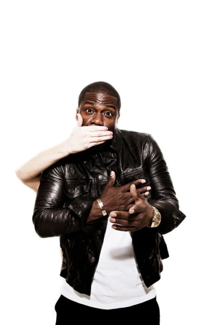 Close-up studio shot of an African-American male with a surprised expression, and a hand covering his mouth wearing a black leather jacket.