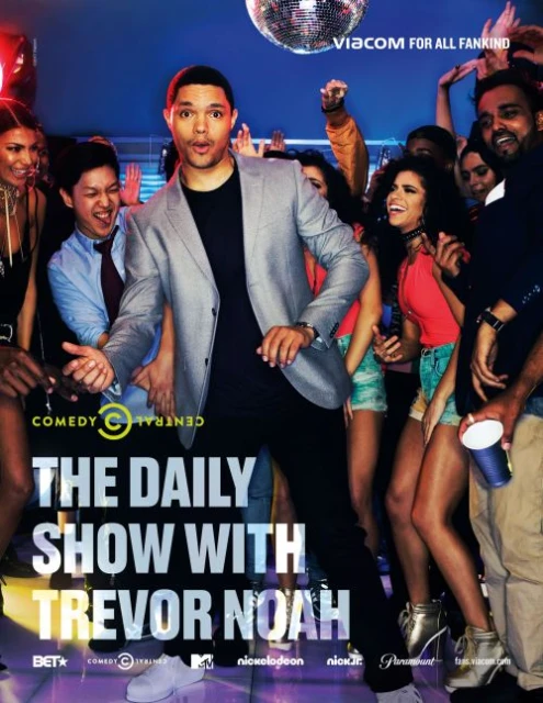 Trevor Noah, in a grey jacket, stands center stage with a diverse crowd in the background. A disco ball hangs above the lively group.