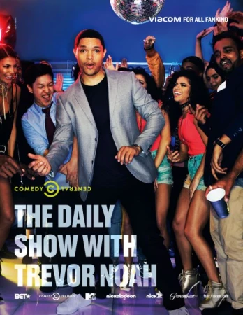 Trevor Noah, in a grey jacket, stands center stage with a diverse crowd in the background. A disco ball hangs above the lively group.