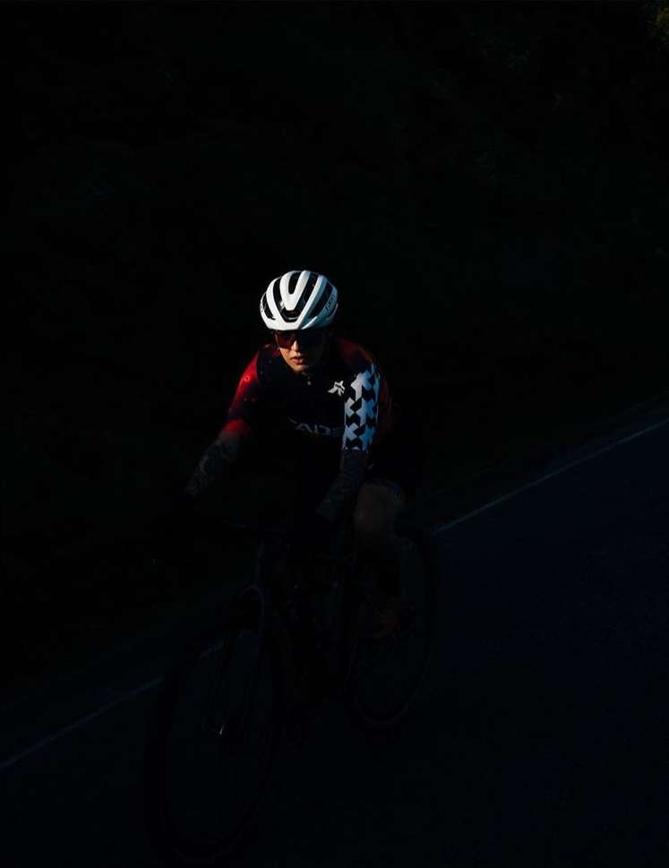 Cyclist wearing helmet and riding a bike in dark setting. Person in cycling gear.