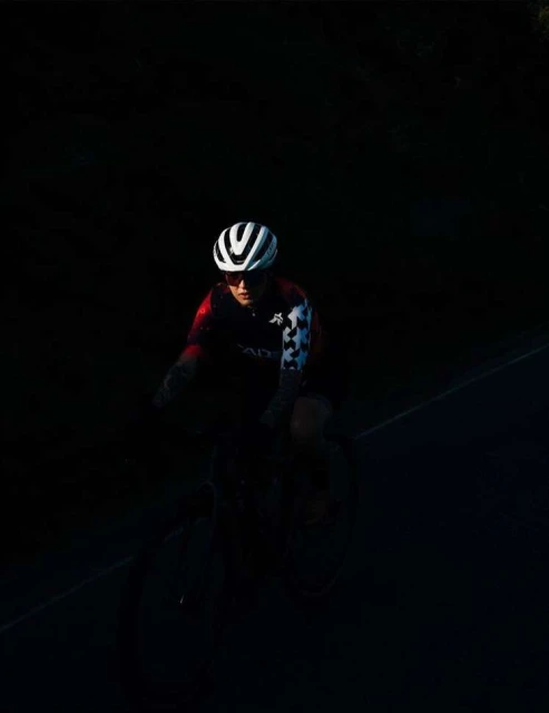 Cyclist wearing helmet and riding a bike in dark setting. Person in cycling gear.
