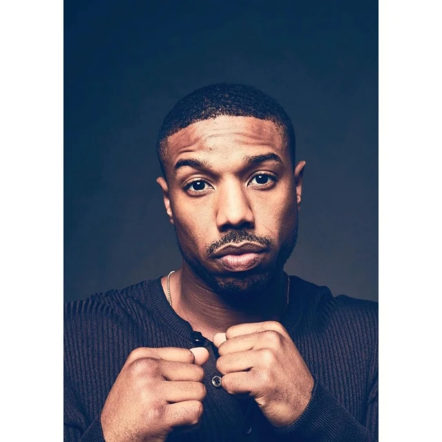 Portrait of a handsome adult male of African descent with a short haircut, wearing a dark top, posing against a dark background.