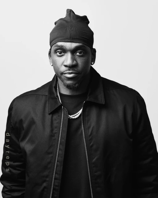 Portrait of a Black adult male wearing a black durag and jacket against a plain white backdrop, looking directly at the camera.