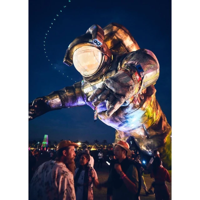 Gigantic astronaut art installation looms over festival crowd at night, captured with a low angle and a dark blue sky backdrop.