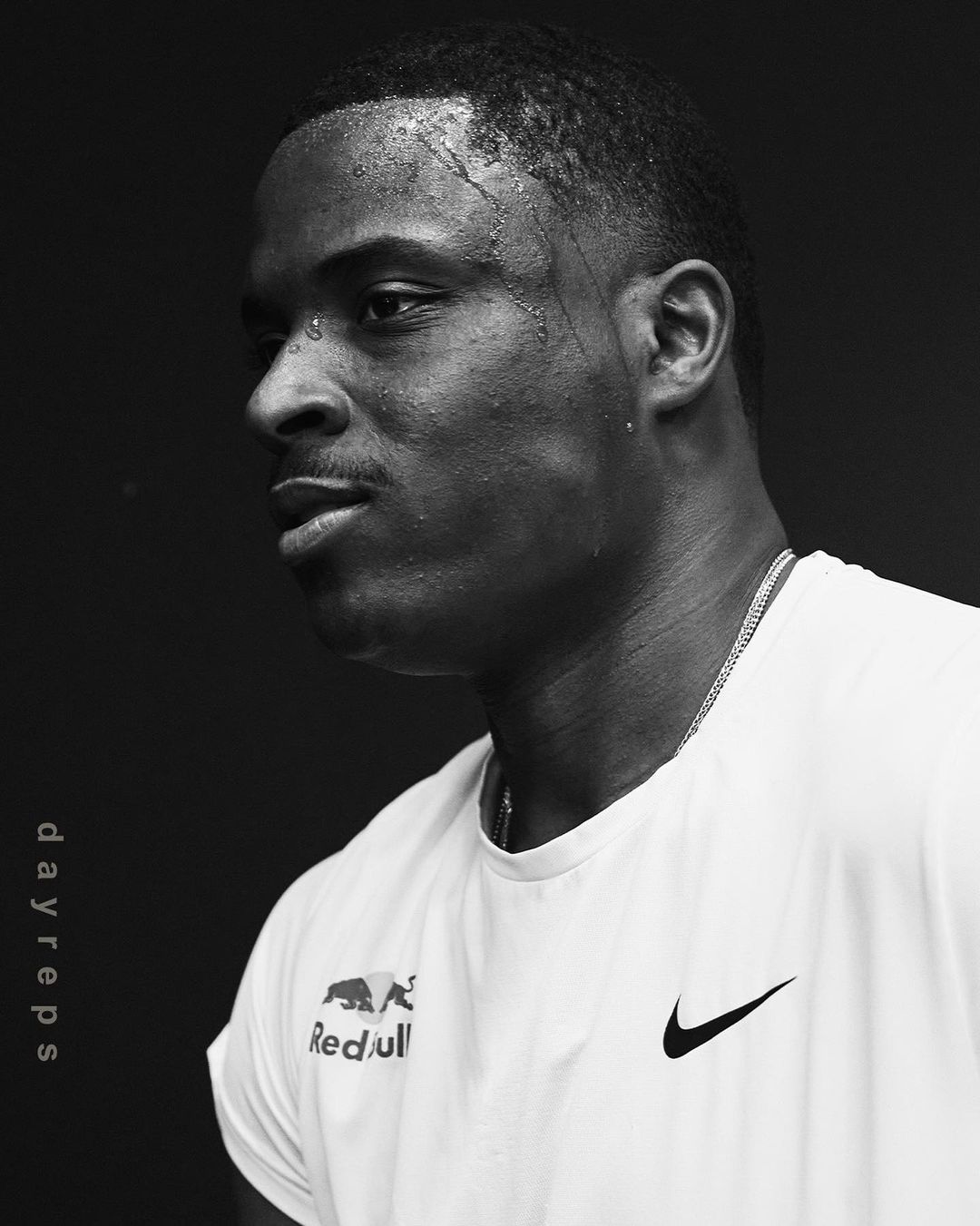 Monochrome portrait of a muscular man with sweat on his face wearing a white t-shirt with the Red Bull logo and a Nike swoosh.