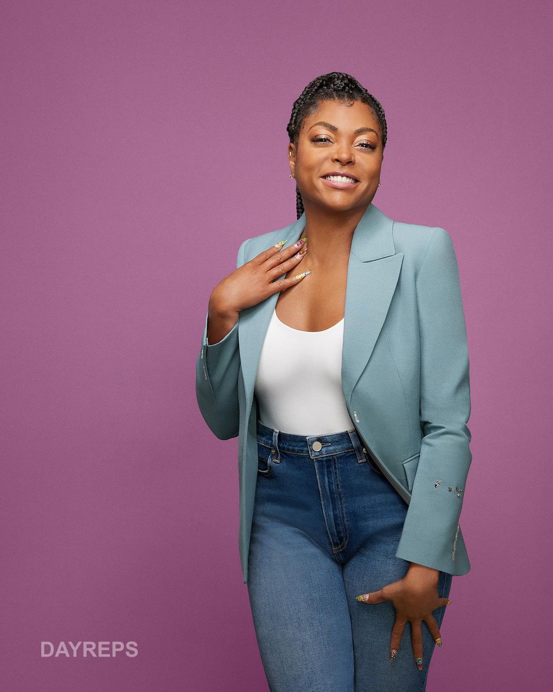 Studio portrait of smiling adult woman in a blazer and jeans against a purple background, looking directly at the camera.
