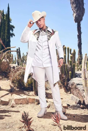 Man in white cowboy hat, coat, and pants poses in arid landscape with cacti and blue sky for fashion, music, or entertainment visual content.