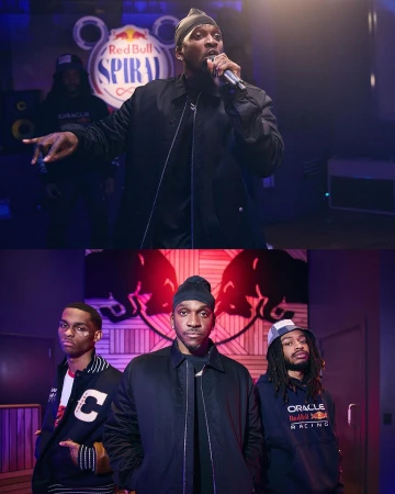 Performance shot featuring a singer with a microphone, backed by two men and brand logos for Red Bull and Oracle in a casual indoor setting.