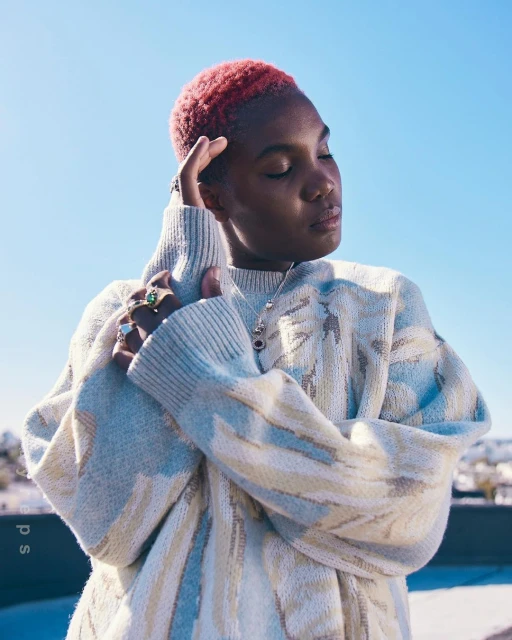 Portrait of an adult female with red hair wearing a patterned sweater against a clear sky with visible rings on her fingers.