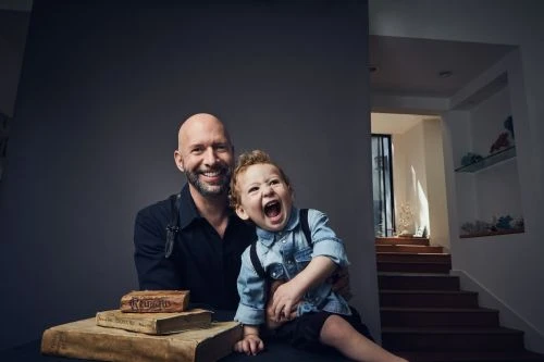 Portrait of a smiling bald man and a laughing toddler in a denim shirt by photographer Koury Angelo