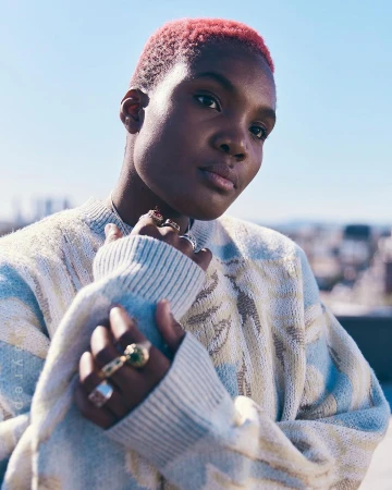 Portrait of a person with short dyed pink hair wearing a textured patterned sweater and several rings by photographer Koury Angelo