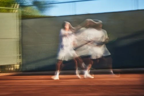 Motion blur of tennis players on an outdoor court. One player in white is hitting a ball, during a match.