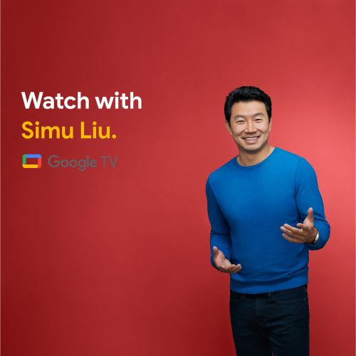 Simu Liu smiles in a medium shot against a red background, wearing a blue sweater in a promotional image for Google TV.