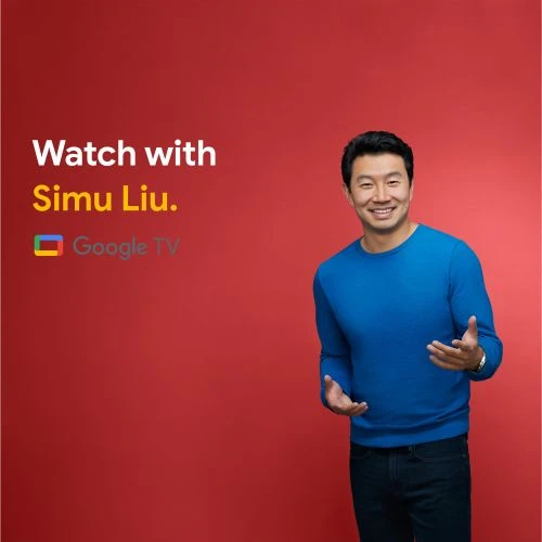 Simu Liu smiles in a medium shot against a red background, wearing a blue sweater in a promotional image for Google TV.