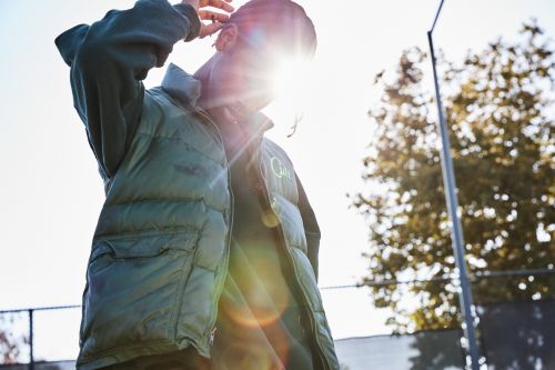Man wearing a green puffer vest standing outdoors in Los Angeles with bright lens flare from the sun behind him.
