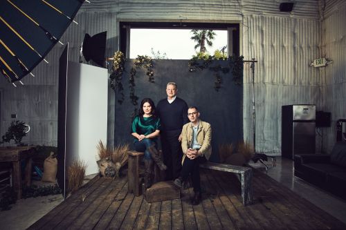 Group portrait of two men and a woman in a studio setting with soft lighting and a rustic, indoor environment, creating a staged image.