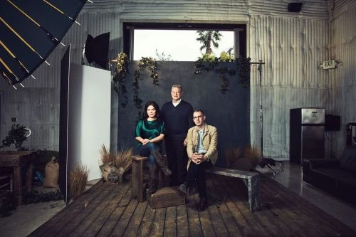 Group portrait of two men and a woman in a studio setting with soft lighting and a rustic, indoor environment, creating a staged image.