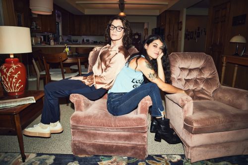 Two people, an adult male and adult female, sitting on pink chairs in an indoor setting. The photo features natural lighting and a home-like backdrop.