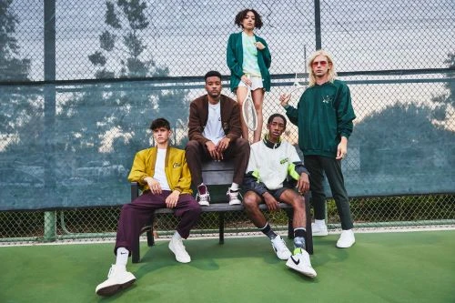 Five diverse young adults pose on a bench in a sportswear fashion shot on a tennis court with athletic shoes, shorts, and jackets.