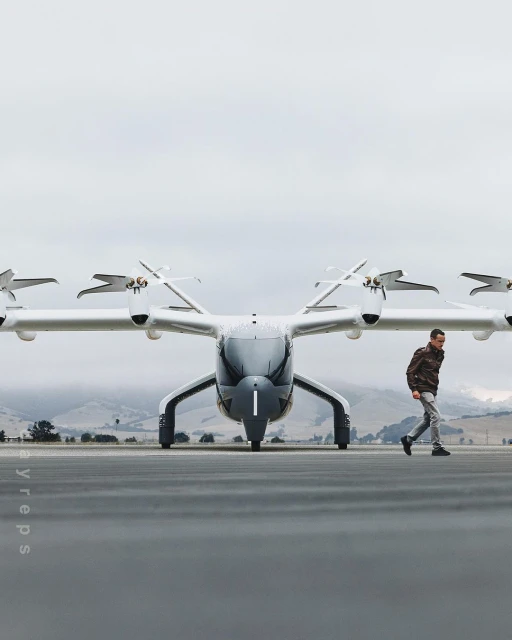 Silver eVTOL aircraft sits on the tarmac as a man walks by. A new form of personal air transportation on a cloudy day.
