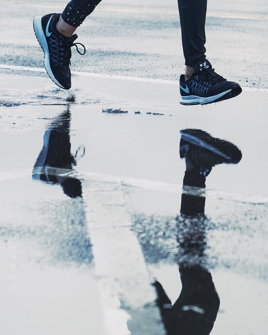 Athletic shoes in motion on wet pavement, reflected in a puddle, promoting running and sports in an urban environment.