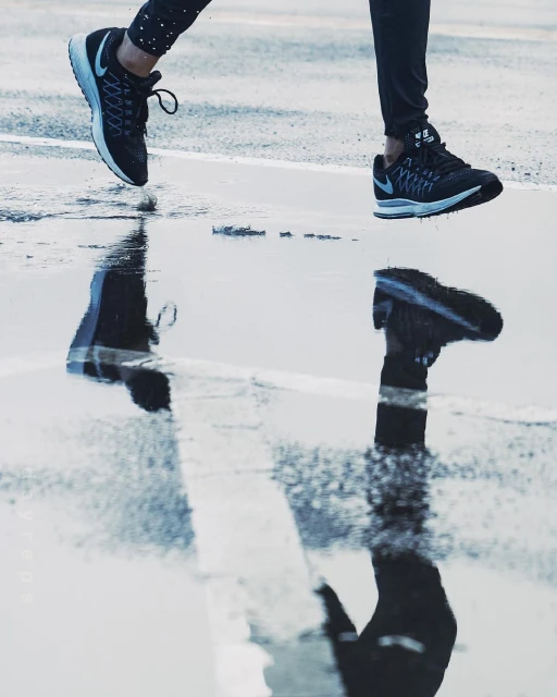 Athletic shoes in motion on wet pavement, reflected in a puddle, promoting running and sports in an urban environment.