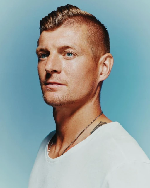 Portrait of an adult man with light brown hair, blue eyes, and a white t-shirt, looking off to the side against a light blue background.