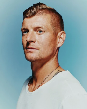 Portrait of an adult man with light brown hair, blue eyes, and a white t-shirt, looking off to the side against a light blue background.