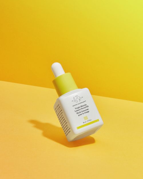 Drunk Elephant Virgin Marula Luxury Facial Oil in white bottle with yellow accents on a yellow background. Beauty and skincare product.