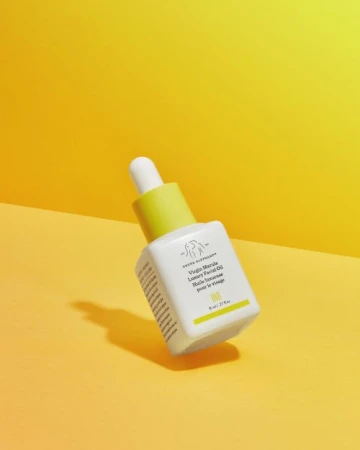 Drunk Elephant Virgin Marula Luxury Facial Oil in white bottle with yellow accents on a yellow background. Beauty and skincare product.