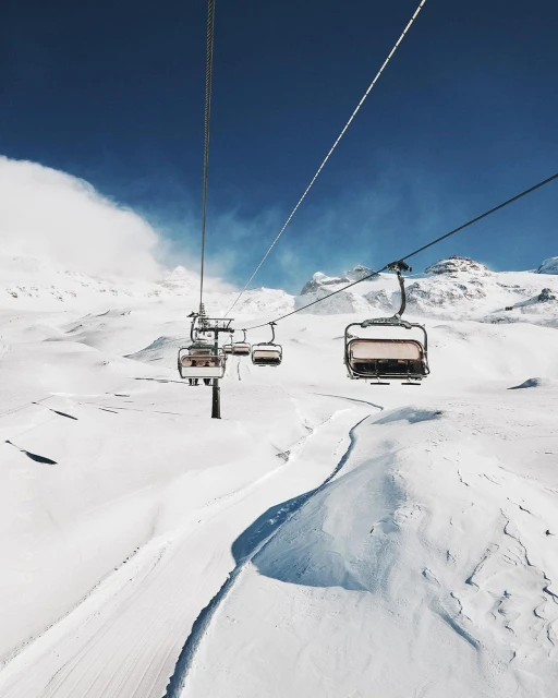 Ski lift chairs ascend over a snowy mountain landscape under a clear blue sky on a sunny day, providing transport for skiers.