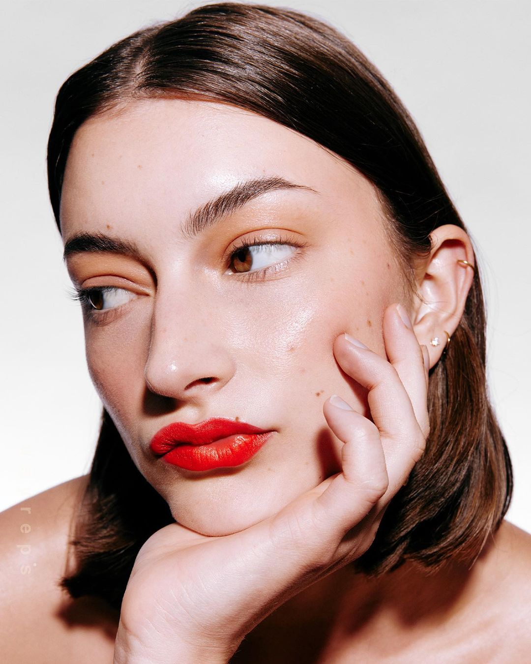 Close-up portrait of an adult woman with red lipstick, light skin, brown hair and looking to the left side of the frame.