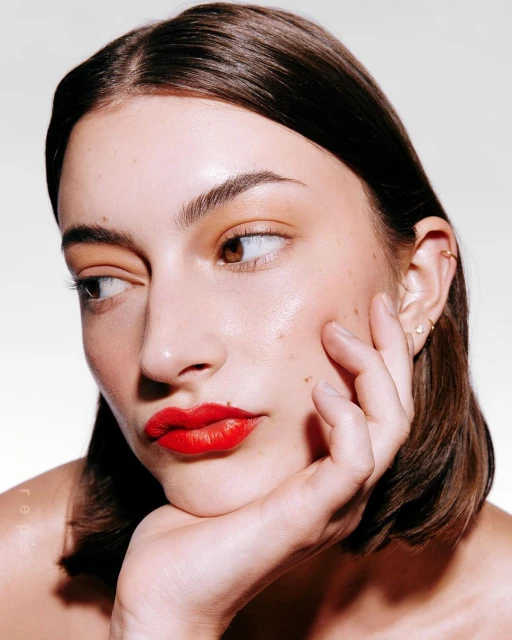 Close-up portrait of an adult woman with red lipstick, light skin, brown hair and looking to the left side of the frame.