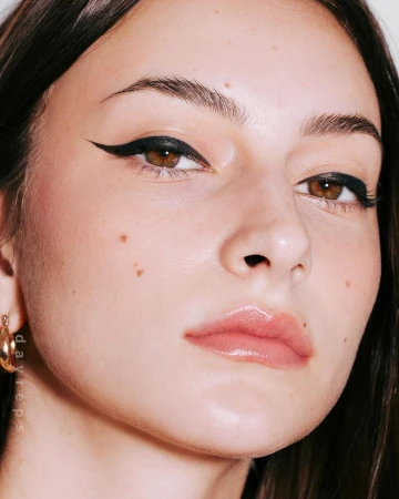 Close-up beauty portrait of a woman wearing sharp black winged eyeliner and glossy nude lips