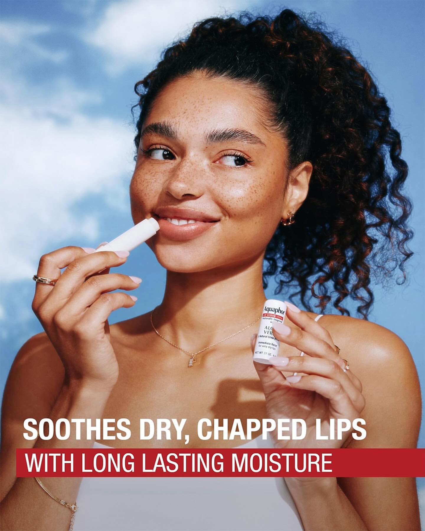 Woman applying lip balm outdoors against a sky background. Close-up shot. Focus on skincare, beauty routine, and lip care.