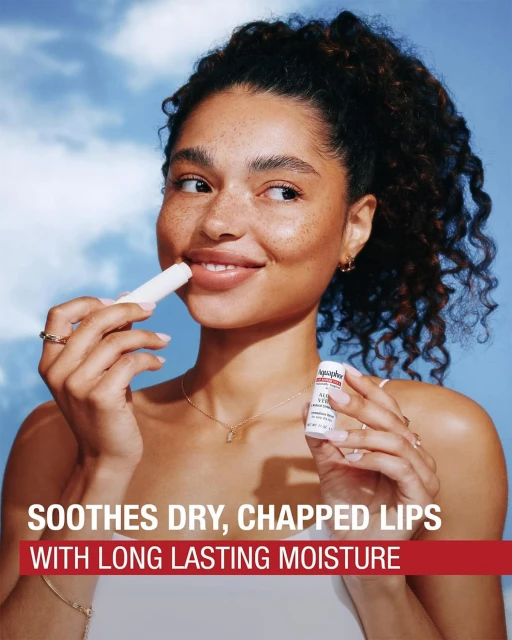 Woman applying lip balm outdoors against a sky background. Close-up shot. Focus on skincare, beauty routine, and lip care.