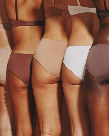 Partial view of five diverse women in matching bra and panty sets posing in a row against a neutral backdrop in a studio setting.