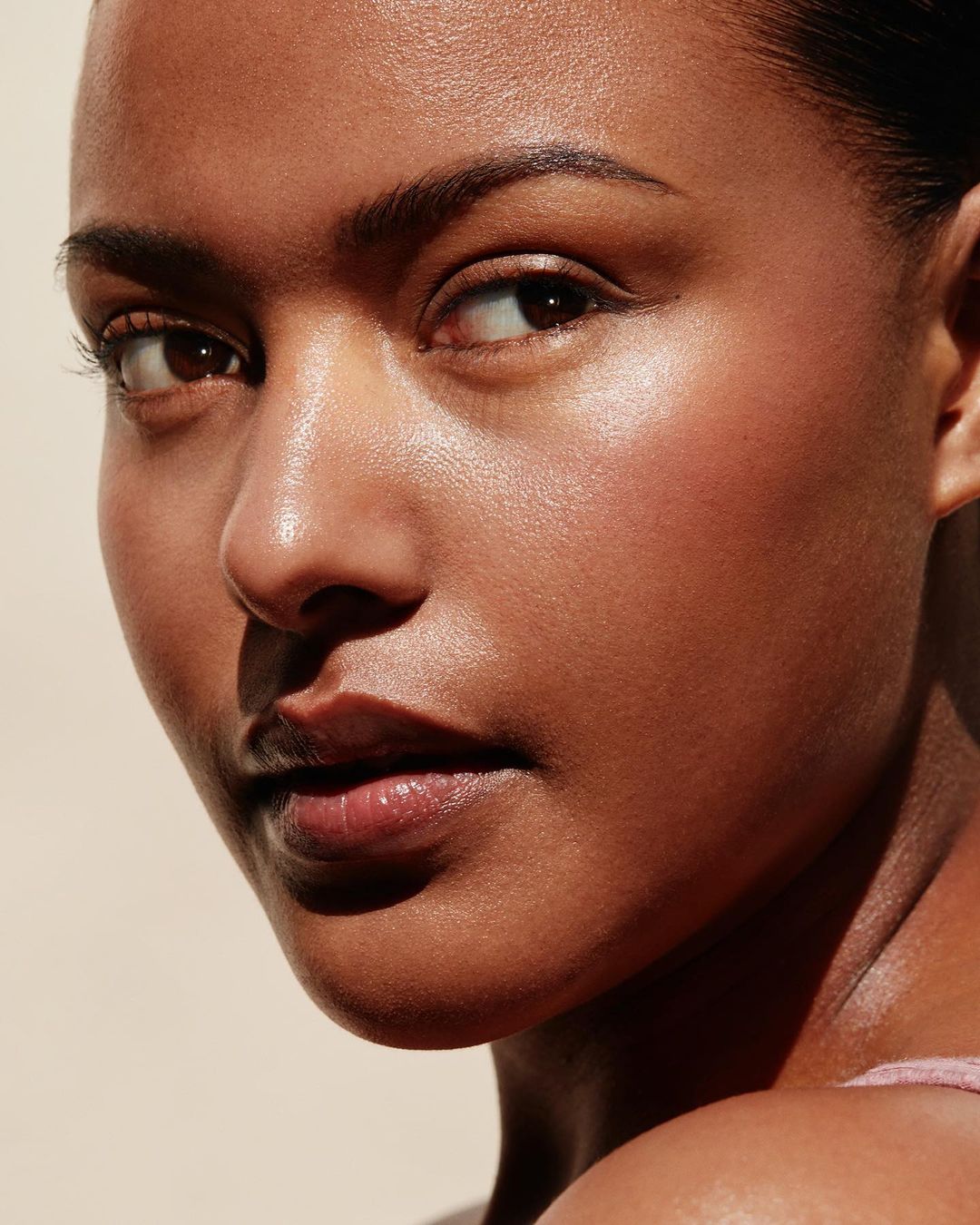 Close-up portrait of a woman with tanned skin and glossy lips bathed in natural light, highlighting the model's smooth skin and facial features.
