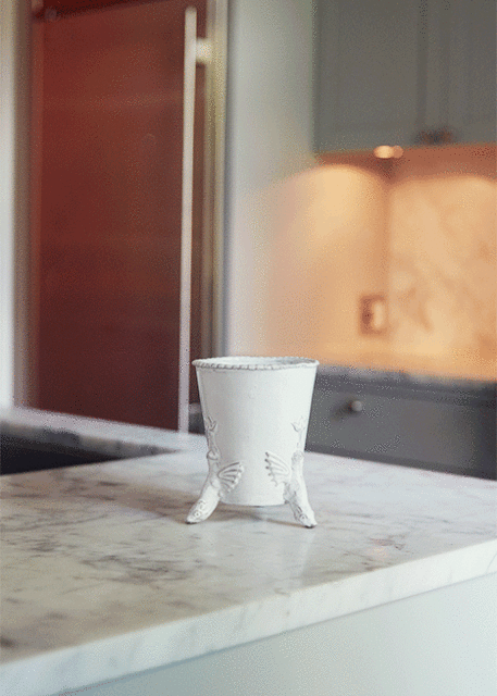 Close-up of a white, decorative vase with a bird motif on a light marble countertop, set against a blurred kitchen background.