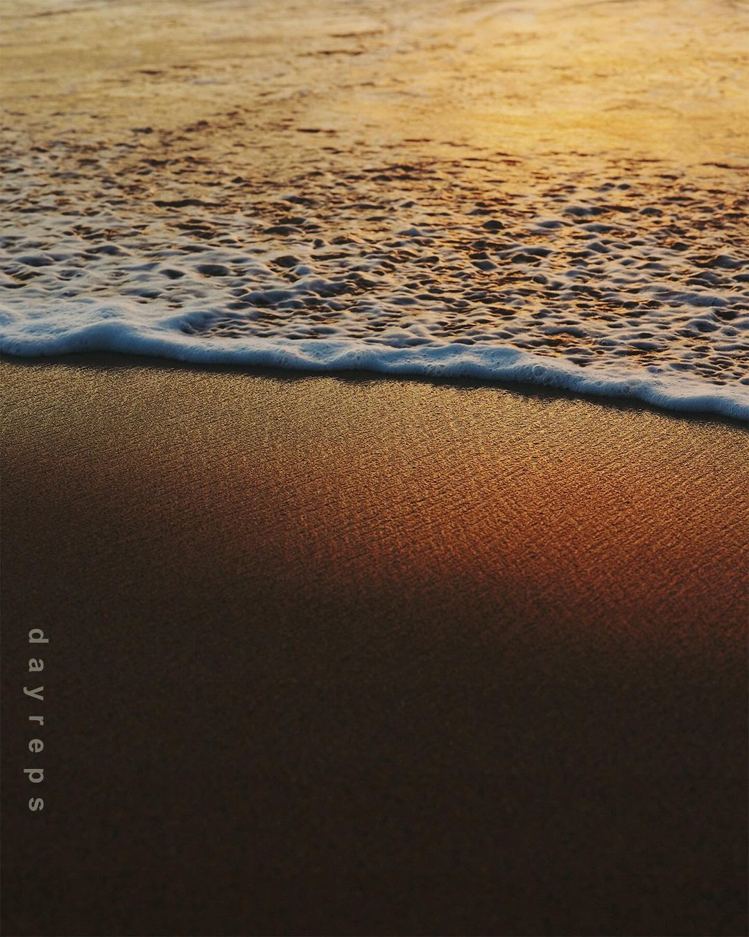 Waves gently rolling onto a sandy beach at sunset, creating a tranquil scene with warm colors and soft textures in the foreground.