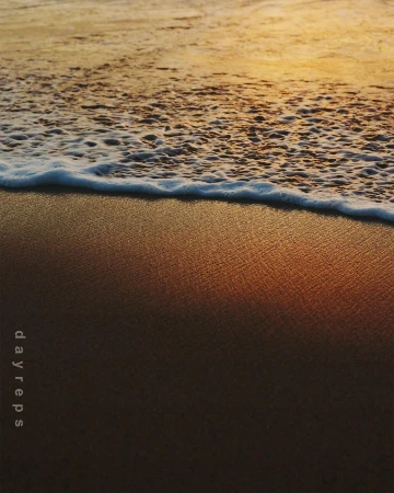 Waves gently rolling onto a sandy beach at sunset, creating a tranquil scene with warm colors and soft textures in the foreground.