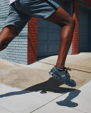 Close-up shot of a runner's legs in athletic shorts and running shoes on a city sidewalk against a blue building.