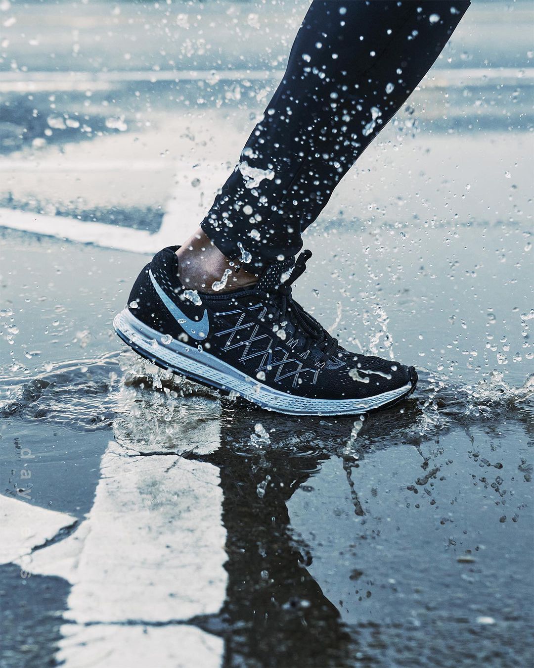 A close-up shot showcases a Nike running shoe splashing in a puddle, highlighting athletic footwear and outdoor activity.
